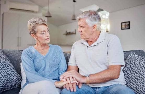 A mature couple sitting closely on a sofa, holding hands and looking at one another